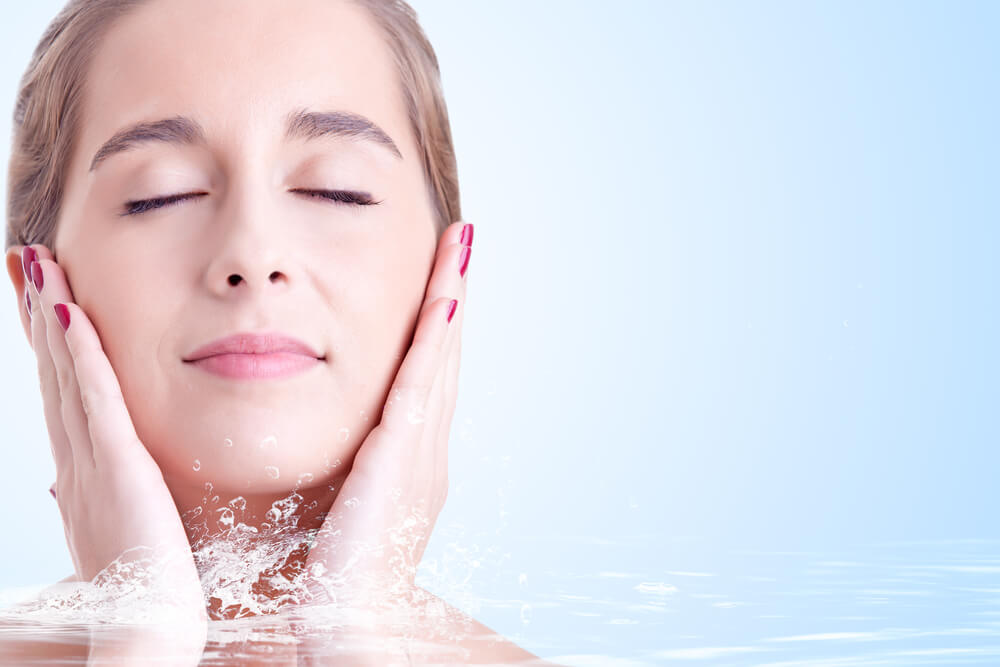 Portrait of young woman touching her face while she smiles in a blue background with water